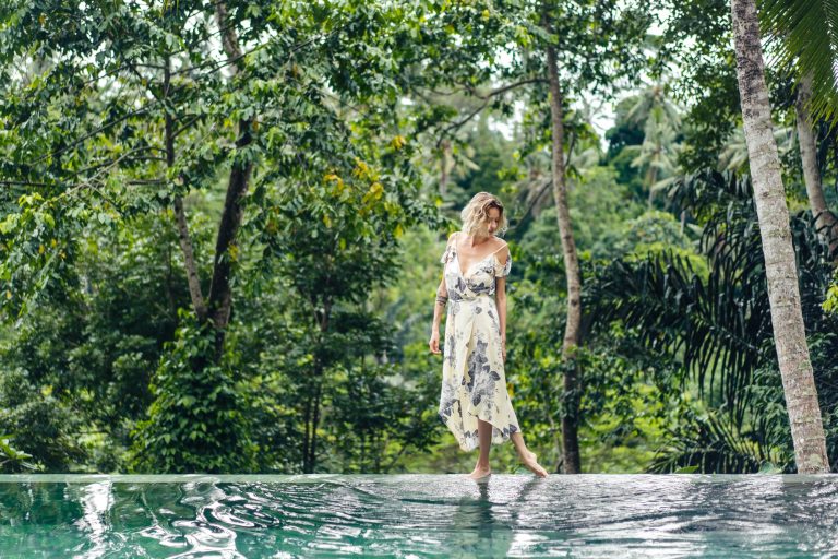 attractive-blond-woman-in-dress-walking-near-swimming-pool-with-green-plants-on-background-ubud-.jpg
